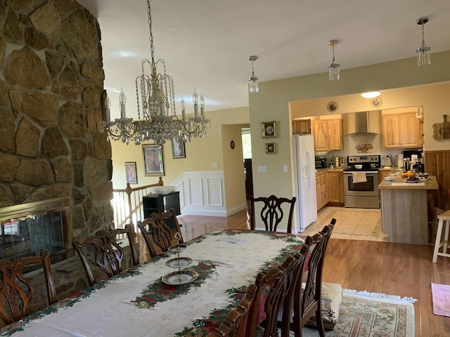 dining space with light wood-style flooring, a notable chandelier, and a stone fireplace