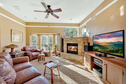 living area featuring ceiling fan and a stone fireplace