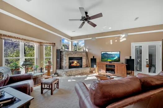 carpeted living room featuring a ceiling fan and a stone fireplace