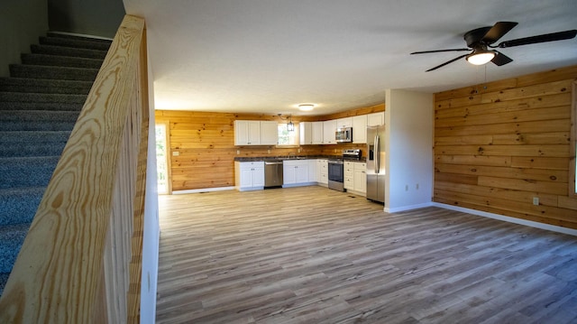 kitchen with ceiling fan, light hardwood / wood-style floors, wooden walls, white cabinets, and appliances with stainless steel finishes