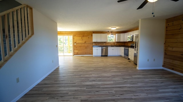 kitchen with white cabinets, appliances with stainless steel finishes, hardwood / wood-style flooring, and wooden walls