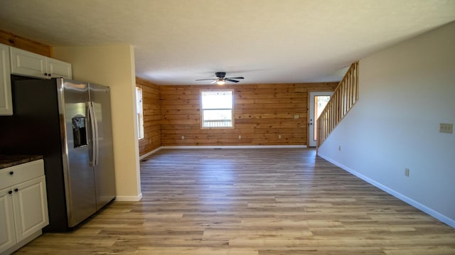 kitchen featuring white cabinetry, ceiling fan, stainless steel fridge, wood walls, and light hardwood / wood-style floors