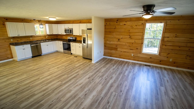 kitchen featuring white cabinets, stainless steel appliances, light hardwood / wood-style floors, and wood walls