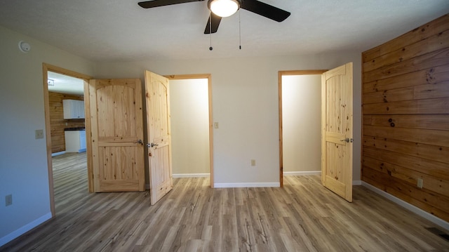 unfurnished bedroom featuring hardwood / wood-style flooring, ceiling fan, and wooden walls