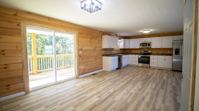 kitchen featuring pendant lighting, white cabinets, wooden walls, light hardwood / wood-style flooring, and stainless steel appliances