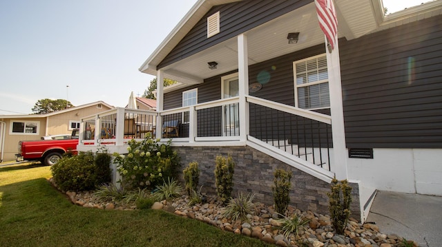 rear view of house with stone siding, covered porch, and a yard