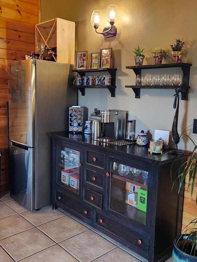 bar with stainless steel fridge, light tile patterned floors, and wood walls