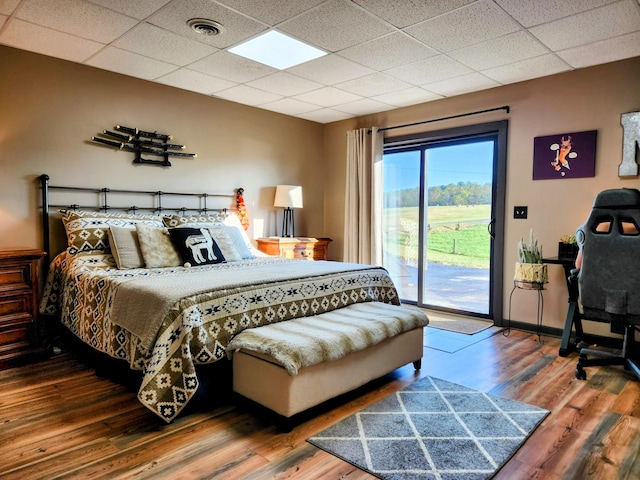 bedroom with access to outside, a paneled ceiling, and hardwood / wood-style flooring