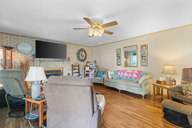 living room featuring light wood-type flooring, a brick fireplace, ceiling fan, and brick wall