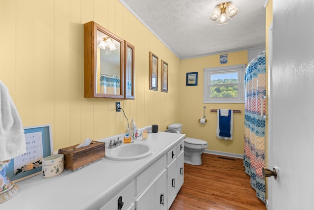 bathroom with ornamental molding, vanity, a textured ceiling, wood-type flooring, and toilet