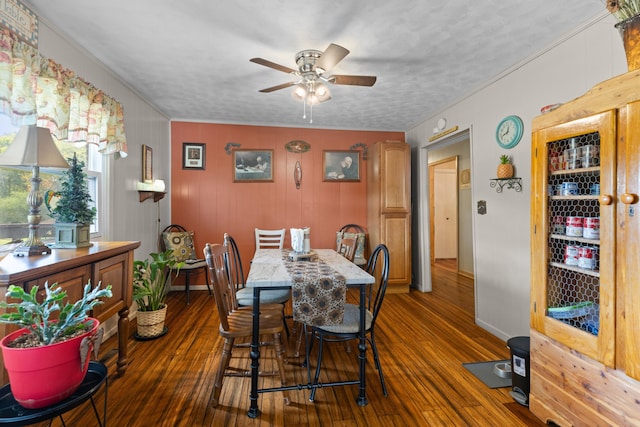 dining area with ceiling fan, wooden walls, dark wood-type flooring, and a textured ceiling