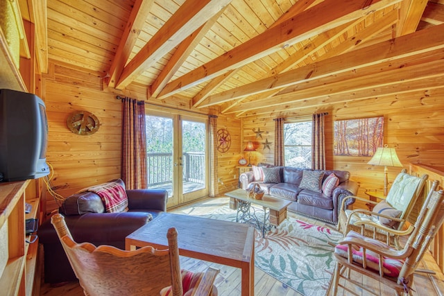 living room with lofted ceiling with beams, a wealth of natural light, wood walls, and french doors