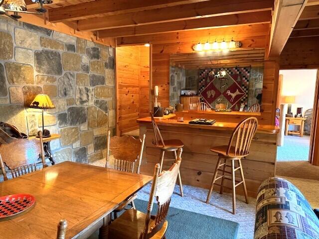 bar featuring beamed ceiling, a fireplace, carpet flooring, and wood walls