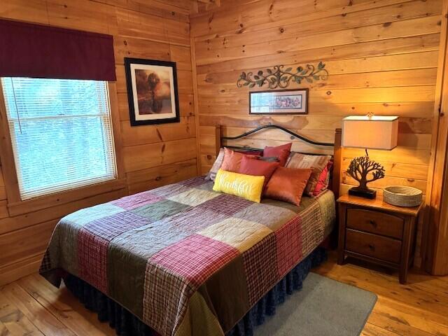 bedroom featuring multiple windows, wooden walls, and light hardwood / wood-style floors