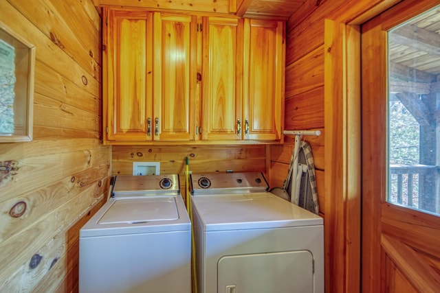 clothes washing area featuring washing machine and dryer, cabinets, and wood walls