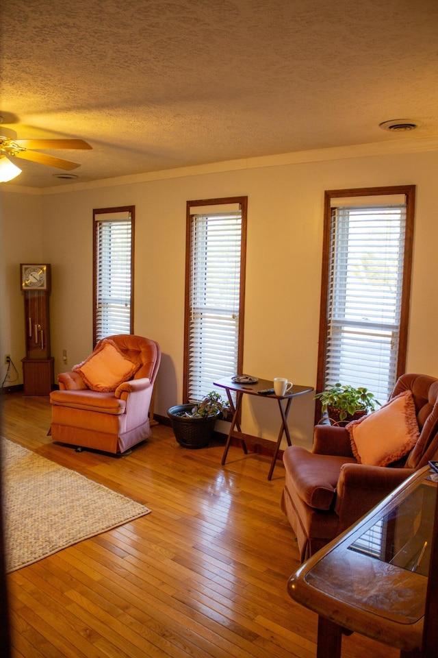 living room with crown molding, light hardwood / wood-style floors, a textured ceiling, and a wealth of natural light