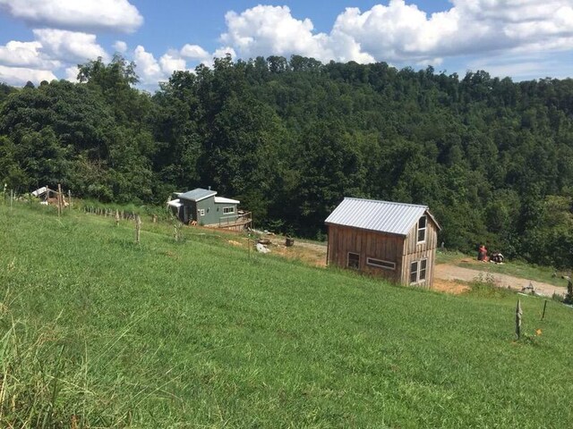 view of yard featuring an outdoor structure, a wooded view, and a rural view