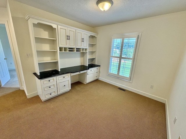 unfurnished office with carpet flooring, built in study area, visible vents, baseboards, and a textured ceiling