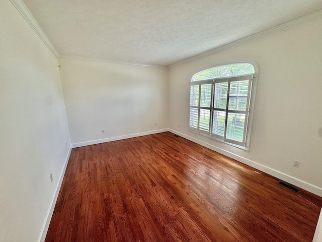 empty room with ornamental molding, visible vents, wood finished floors, and baseboards