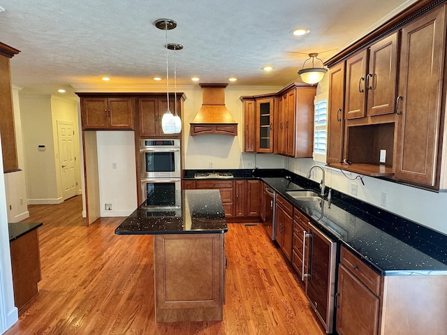 kitchen featuring appliances with stainless steel finishes, custom exhaust hood, sink, a center island, and hanging light fixtures