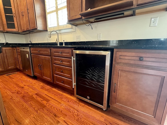 kitchen featuring sink, dishwasher, beverage cooler, dark stone countertops, and hardwood / wood-style flooring