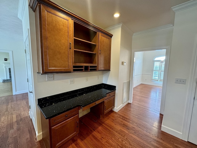 kitchen with dark hardwood / wood-style flooring, built in desk, dark stone counters, and crown molding