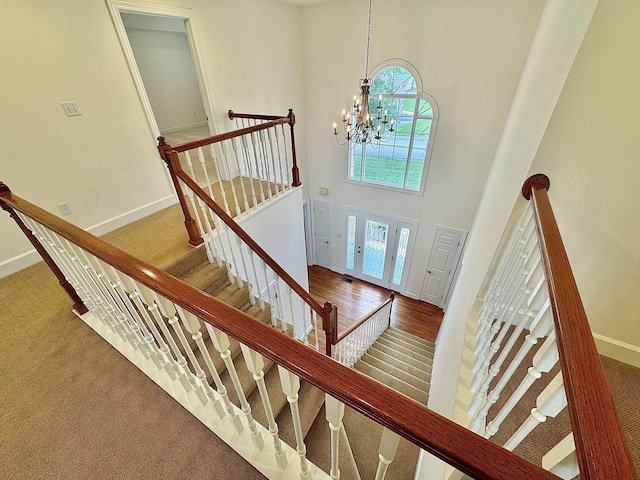 staircase featuring carpet, a chandelier, baseboards, and a high ceiling