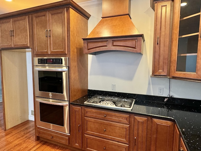 kitchen with appliances with stainless steel finishes, light hardwood / wood-style flooring, custom range hood, and dark stone countertops