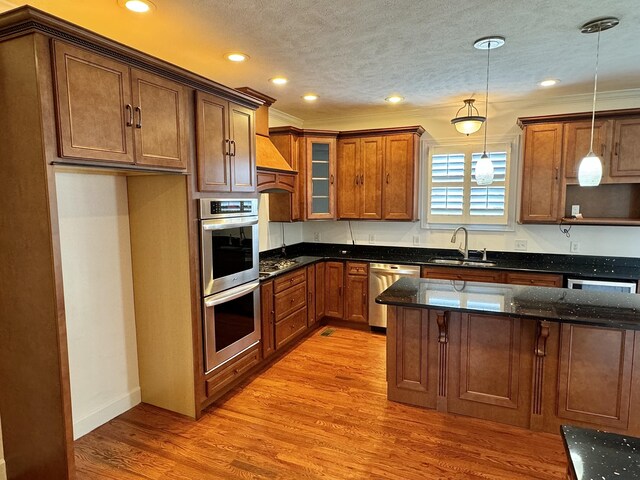 kitchen with sink, light hardwood / wood-style flooring, dark stone countertops, pendant lighting, and appliances with stainless steel finishes