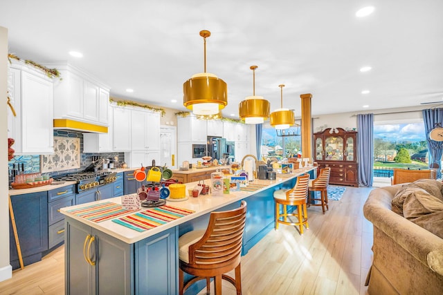 kitchen with stainless steel appliances, a large island with sink, pendant lighting, white cabinetry, and a breakfast bar area