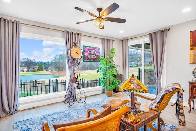 sitting room with wood-type flooring, a water view, and ceiling fan
