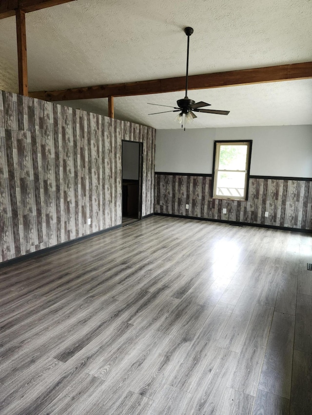 unfurnished living room with hardwood / wood-style floors, a textured ceiling, ceiling fan, and vaulted ceiling with beams