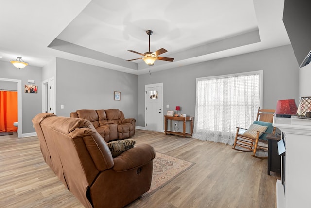 living room featuring a raised ceiling, ceiling fan, and light wood-type flooring