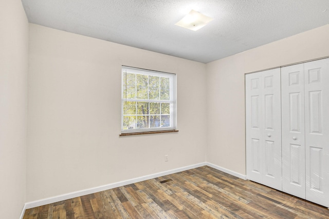 unfurnished bedroom with a textured ceiling, dark hardwood / wood-style floors, and a closet