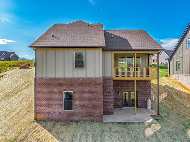 rear view of property featuring a lawn, french doors, brick siding, and a patio