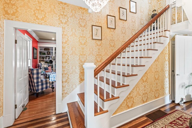 stairs with hardwood / wood-style floors, built in shelves, ornamental molding, and a chandelier