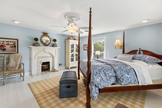 bedroom featuring ceiling fan, light hardwood / wood-style floors, and a fireplace