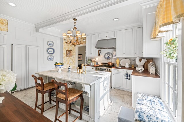 kitchen featuring stainless steel stove, decorative light fixtures, a kitchen bar, white cabinets, and ornamental molding