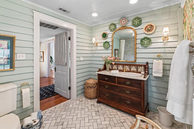 bathroom featuring wooden walls, toilet, vanity, and ornamental molding