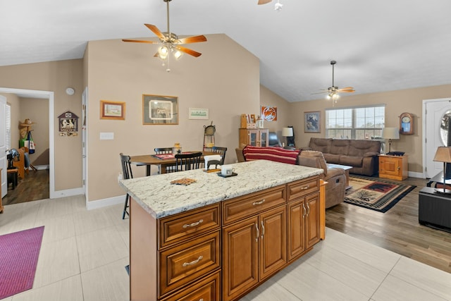 kitchen with light stone counters, vaulted ceiling, light hardwood / wood-style floors, a kitchen island, and ceiling fan