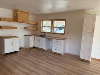 kitchen featuring white cabinetry, wood finished floors, a sink, and open shelves