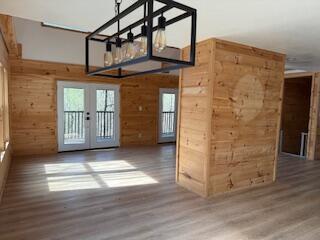 empty room with wood walls, french doors, an inviting chandelier, and wood finished floors