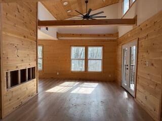 unfurnished living room with ceiling fan, high vaulted ceiling, wood finished floors, and wood walls
