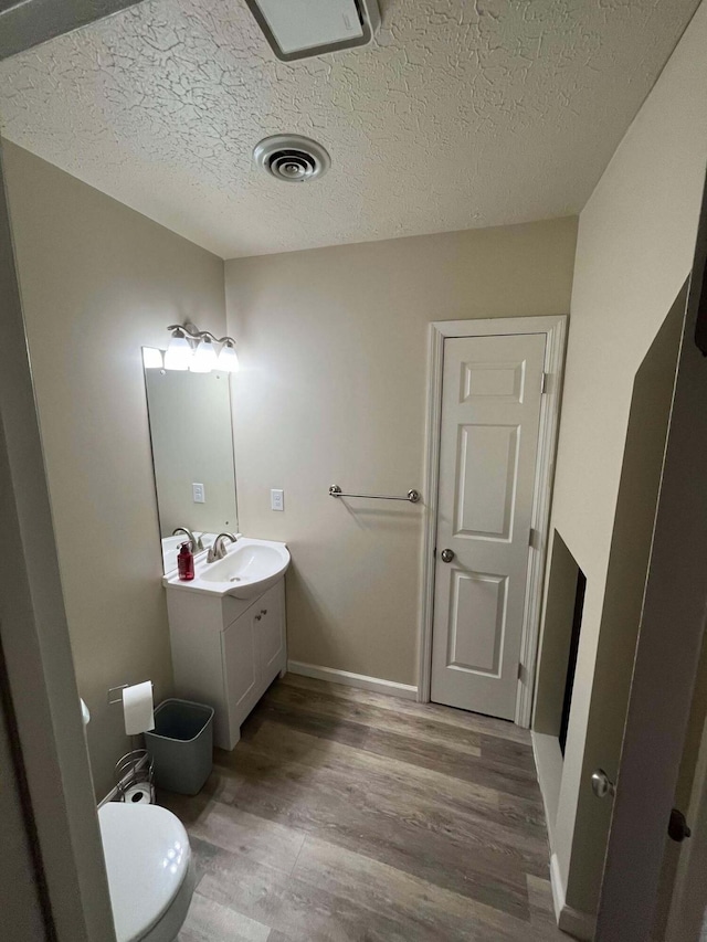 bathroom with hardwood / wood-style flooring, vanity, toilet, and a textured ceiling