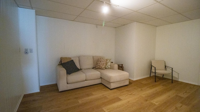 living area with light wood finished floors, a paneled ceiling, and baseboards