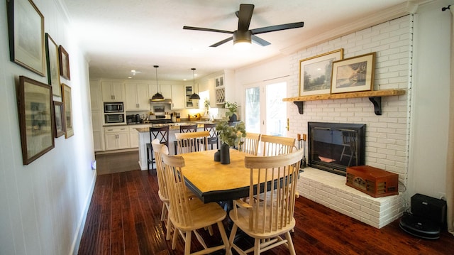 dining room featuring dark wood-type flooring, a fireplace, a ceiling fan, and crown molding