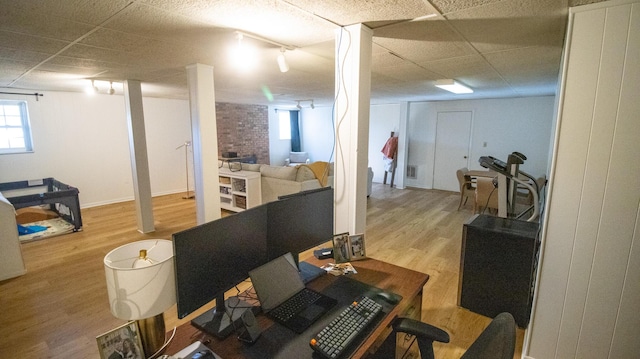 basement featuring a drop ceiling, brick wall, and wood finished floors