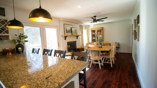 dining room featuring a ceiling fan, crown molding, a brick fireplace, and dark wood-style floors