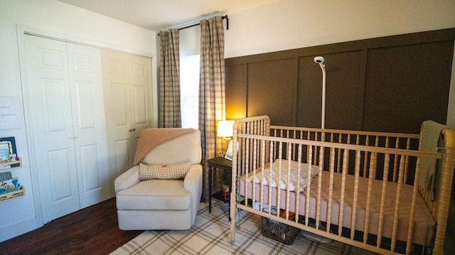 bedroom featuring wood finished floors, a wainscoted wall, a crib, a closet, and a decorative wall