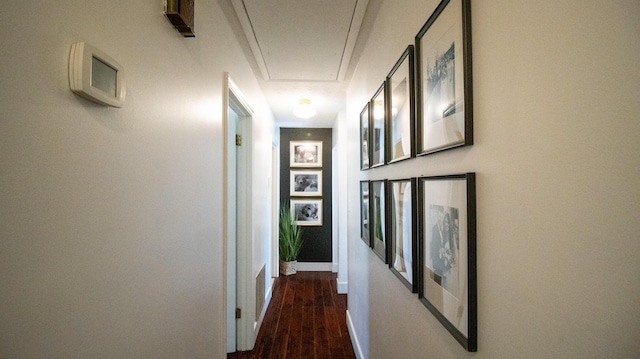 hall featuring baseboards, attic access, and wood finished floors